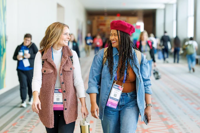 A photo of two women smiling at one another while walking. 