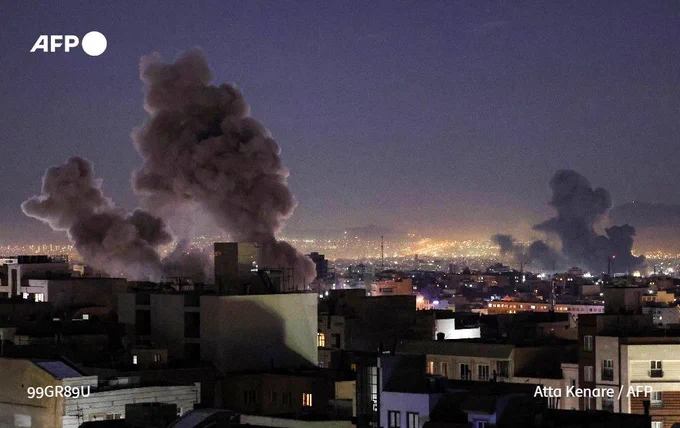 Smoke rising over buildings at night with lights in the background