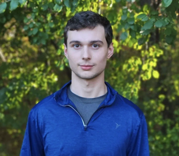 young man with short dark hair, deep blue pullover in front of trees