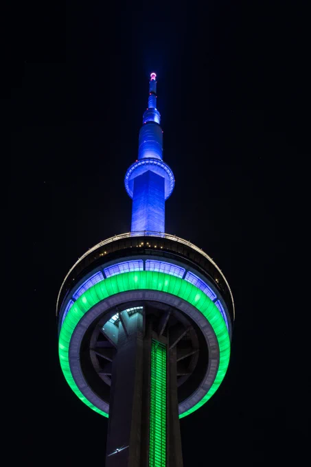 Closeup of the CN Tower at night lit blue and green / Gros plan de la Tour CN illuminée en bleu et vert la nuit 