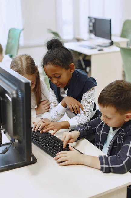 Three children work together on a computer in a school lab, learning and collaborating.