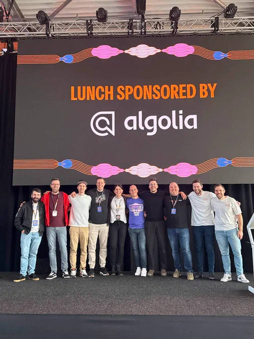 A group of people poses on stage, with a backdrop announcing lunch sponsorship by Algolia, at a Laracon event.