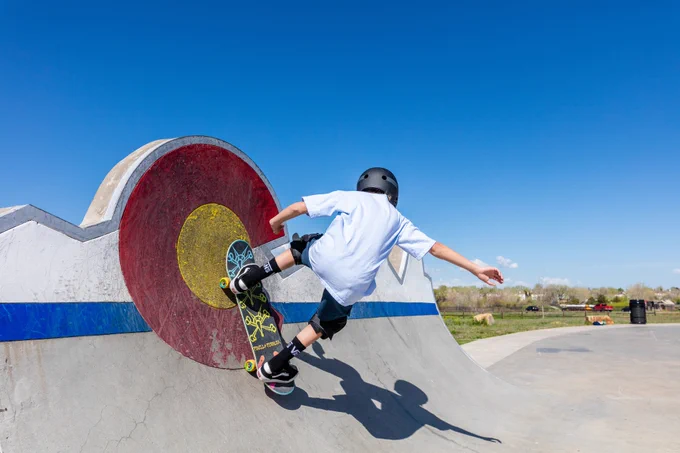 A teenager skateboards over a large Colorado "C" at an outdoor skate park. 