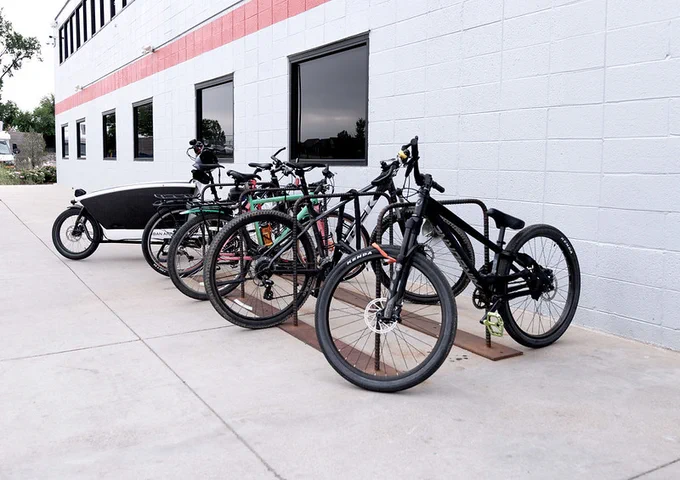 Various bicycles line a bike rack next to a white brick building.