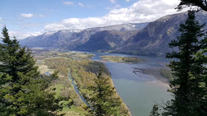 Near Beacon Rock, Washington, USA, river running through a green valley, with plains on the left side and steep mountains with a dusting of snow on the right.