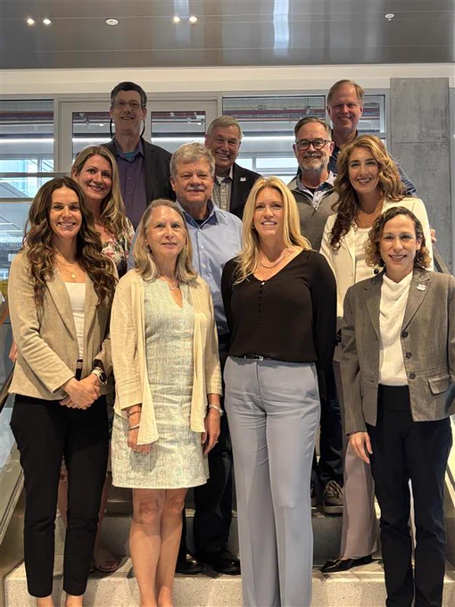 Group photo of the UF Industrial and Systems Engineering Department Advisory Board standing together indoors during their spring meeting. Board members and department leaders are arranged in rows on a staircase inside a modern academic building.