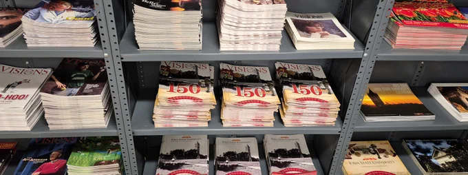 Piles of various editions of Visions and Iowa Stater magazines piled on shelves at Surplus.