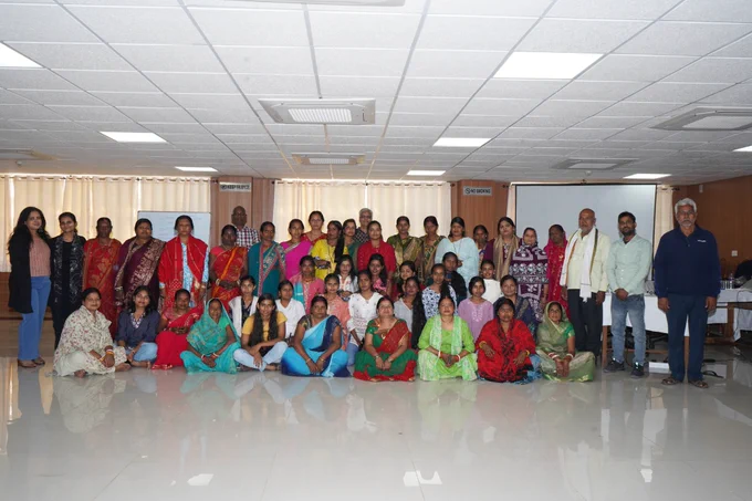 A large group of women and a few men pose together with CREA staff for a group photo inside a hall.