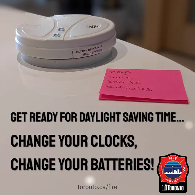 White smoke detector placed on a table next to a pink sticky note listing eggs, milk, snacks, and batteries.