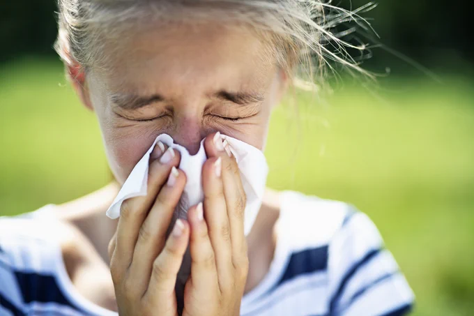 Teenage girl sneezing into a tissue in a park.