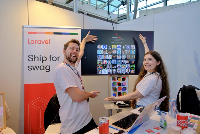 Leah Thompson and James Brooks posing in front of the Laravel Ship for Swag booth sign.