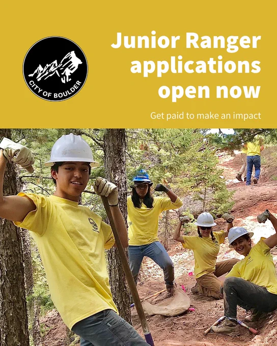 Group of young volunteers in yellow shirts and white helmets flexing muscles during outdoor trail work in a forested area.