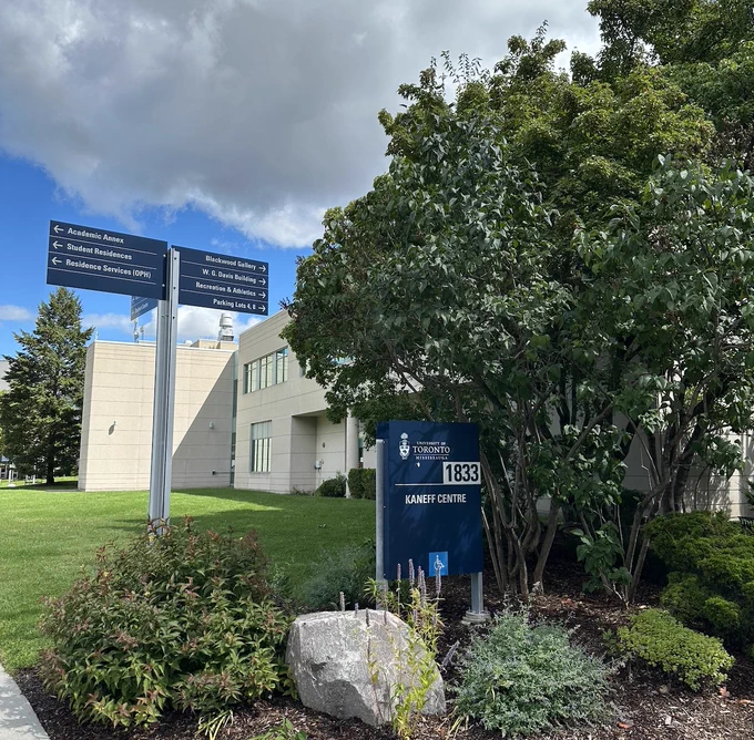 Exterior of the University of Toronto Mississauga's Kaneff Centre.The building is surrounded by greenery and there are directional signs pointing to other campus areas. 