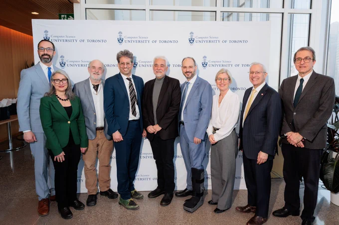 Nine adults in business attire stand shoulder to shoulder in front of a University of Toronto Department of Computer Science backdrop, posing for a formal group photo at an indoor event space.
