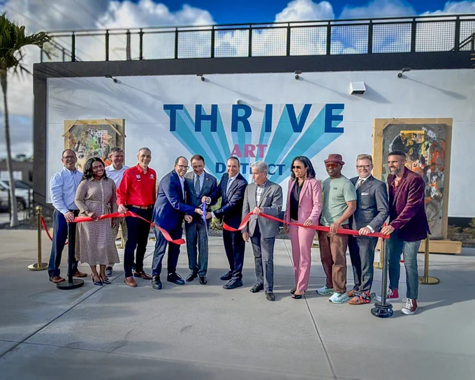 Group of diverse people cutting a red ribbon at the Thrive Art District opening event outdoors.