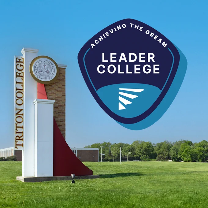 A monument sign for Triton College is situated on a grassy area under a clear blue sky. Next to it, a large emblem reads "Achieving the Dream Leader College." Trees and buildings are visible in the background.