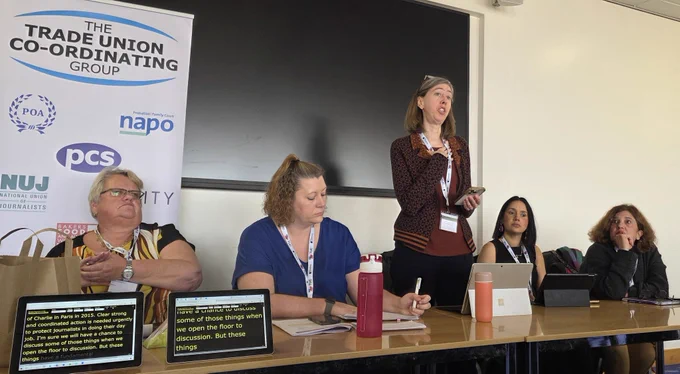 NUJ GS Laura stands as she delivers her speech, flanked by two women trade unionists on each side and the tucg banner in the background 