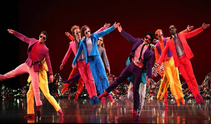 Performers in colourful suits and sunglasses dancing on stage.