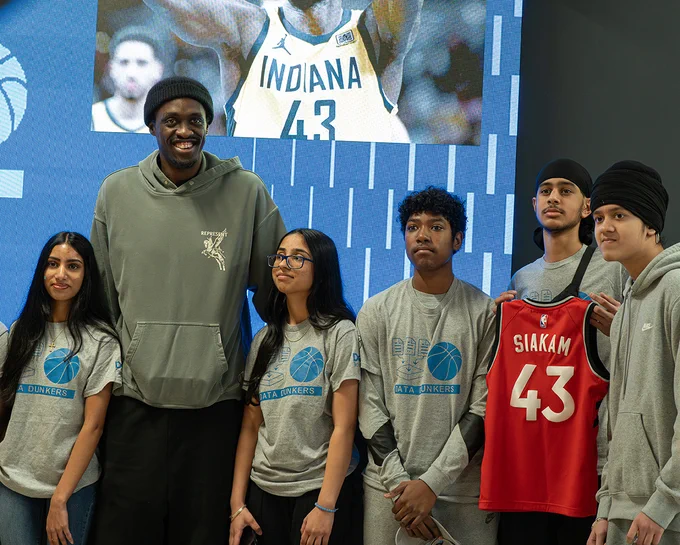 A person stands with a group of youth. One of them is holding up a jersey with the name Siakam and the number 43 on the back.
