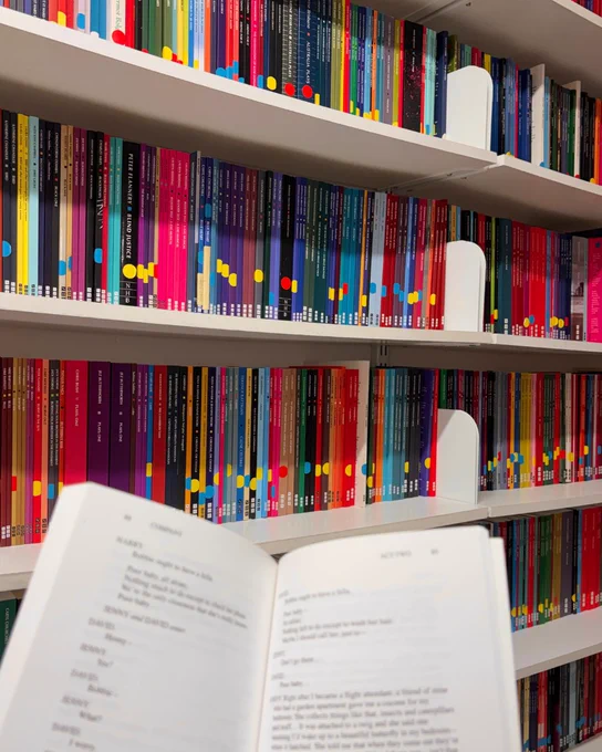 Playscript open in front of shelves full of playscripts.
