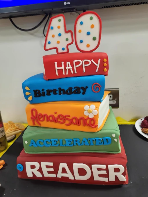 A tiered cake designed to resemble stacked books with the words "40 Happy Birthday Renaissance Accelerated Reader." The books are decorated in bright colors with polka dots.