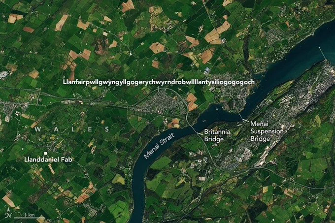 The long-named town in Wales appears as a gray patch amidst a bucolic image with green farmland bordering the Menai Strait. Some towns and key features are labeled.