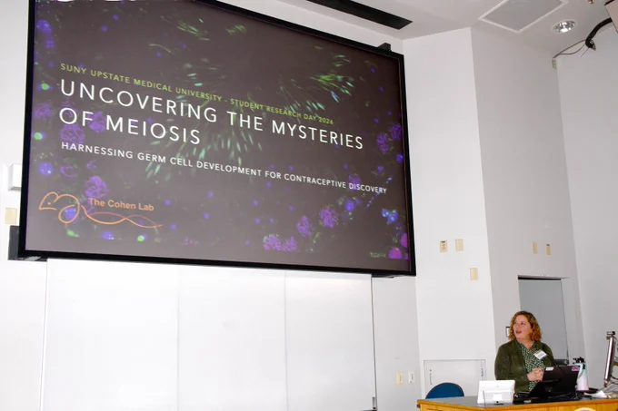 A presentation slide reads “SUNY Upstate Medical University Student Research Day 2026: Uncovering the Mysteries of Meiosis – Harnessing Germ Cell Development for Contraceptive Discovery” as a speaker stands at the podium.