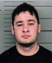 Close up photo of person with dark hair wearing a black shirt with a striped background.
