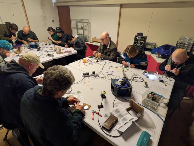 Soldering workshop at TOG Hackerspace with participants seated around tables, focused on assembling electronics kits with soldering irons and tools