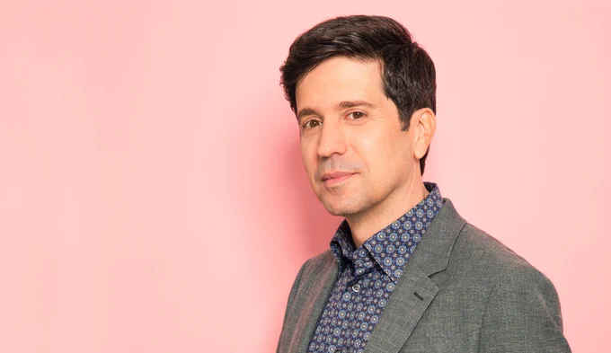Portrait of John Piscitello standing in front of a blush-colored wall.
