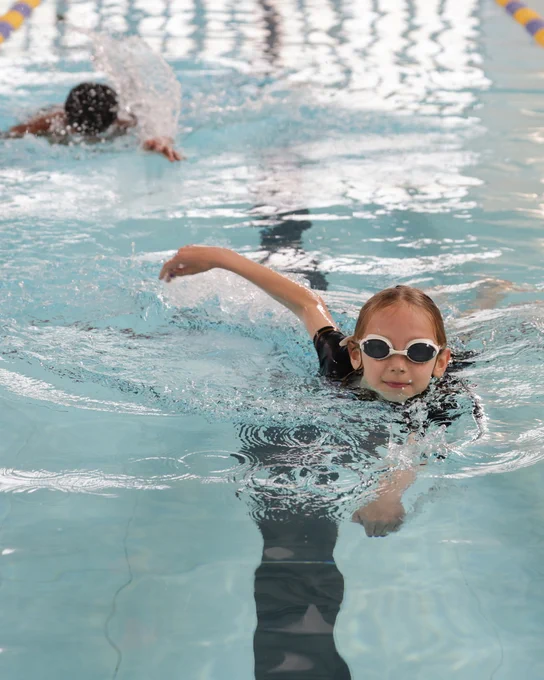 A photo of a young girl swimming in a swimming pool whilst wearing goggles.