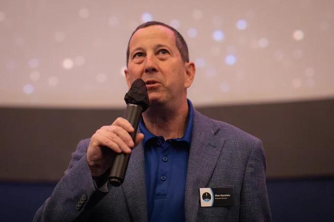 Event photo from AIMLX26. Image depicts a man holding a microphone in front of a starry background.
