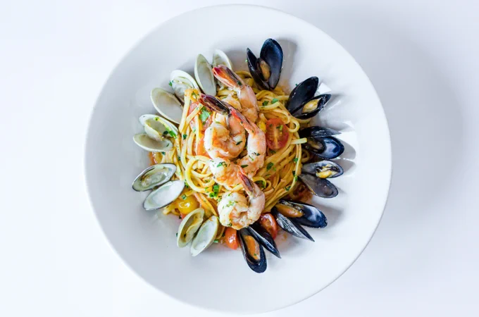 Plated pasta dish with linguine topped with shrimp, mussels, clams, cherry tomatoes in white bowl.