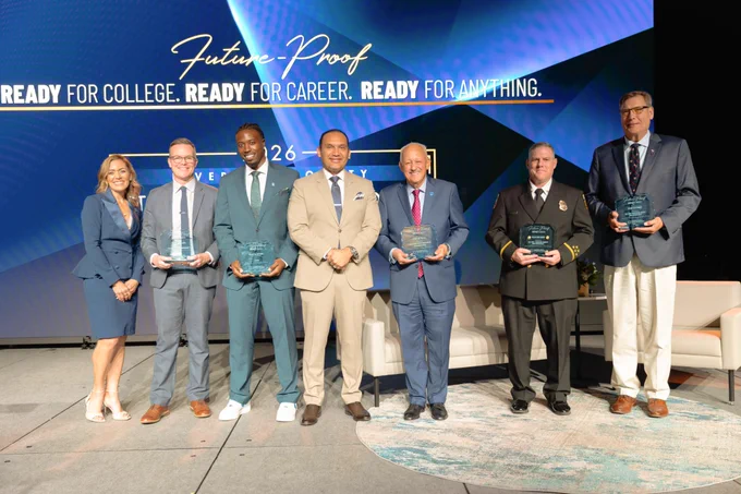 Seven people pose on a stage at an awards event, several holding glass plaques. Behind them, a large blue screen reads “Future-Proof” and “READY FOR COLLEGE. READY FOR CAREER. READY FOR ANYTHING."
