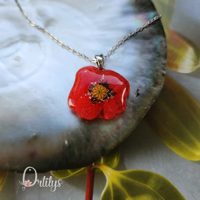 un collier argenté, le médaillon est une fleur de coquelicot stylisée, faite avec des pétales rouges d'hortensia, et un coeur de graines de coquelicot
