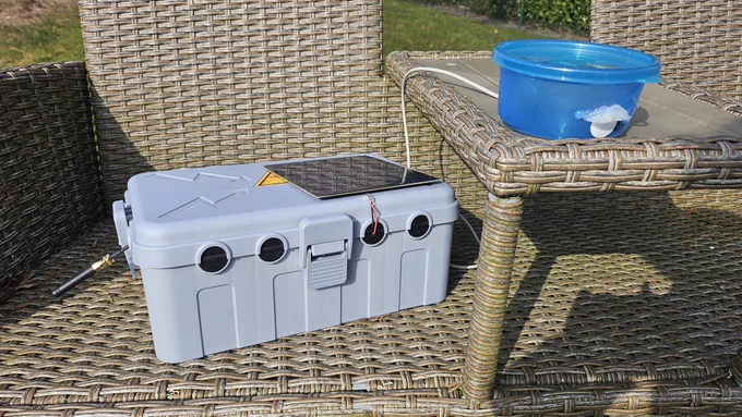 Graue Elektrobox mit Antenne und Solarpanel, daneben eine blaue Tupperdose mit Mikrofon hinter einer Membran