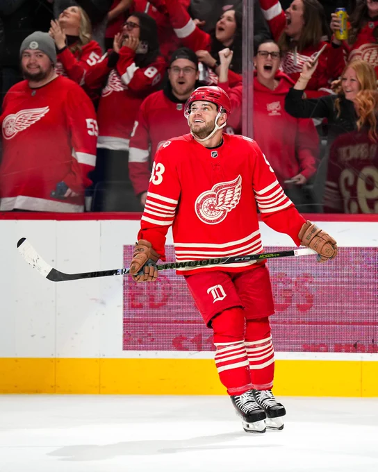 Alex DeBrincat on ice smiling in a Red Wings uniform
