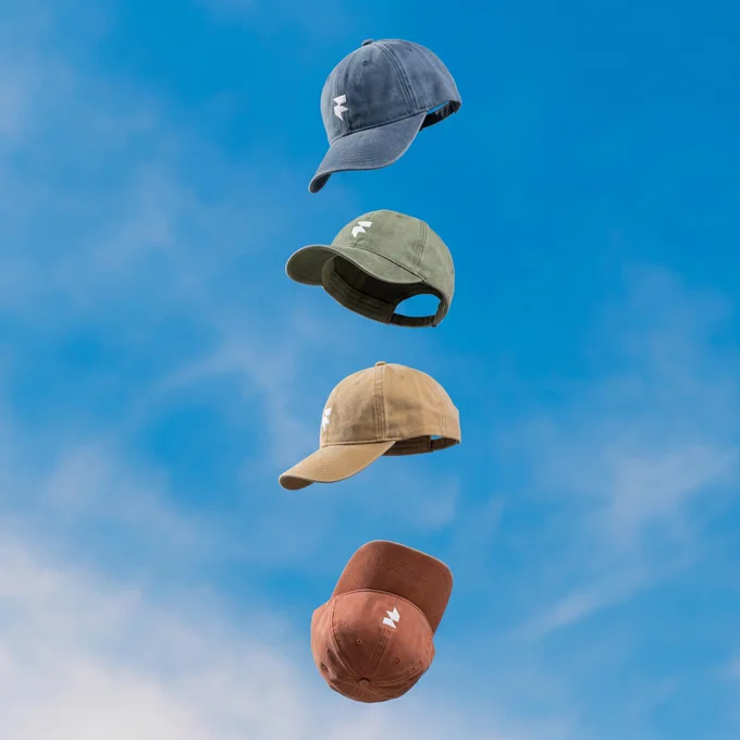 Four caps in different colors float against a bright blue sky, showcasing a variety of styles above a soft, clouded backdrop.