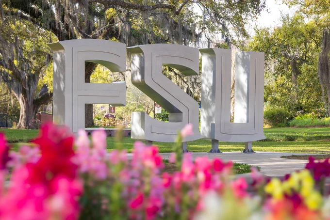 Statue of the FSU Logo with flowers of various colors blurred in the foreground