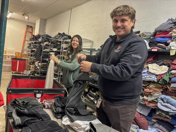 Two volunteers smile as they sort clothing. 