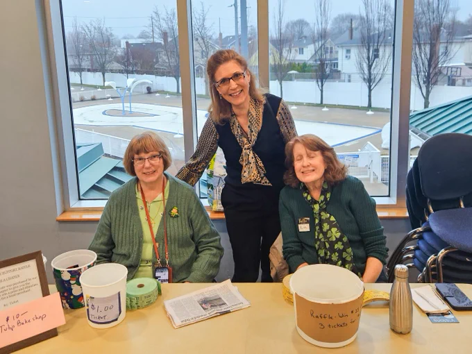 A group of three women sit at a desk and smile to the camera.