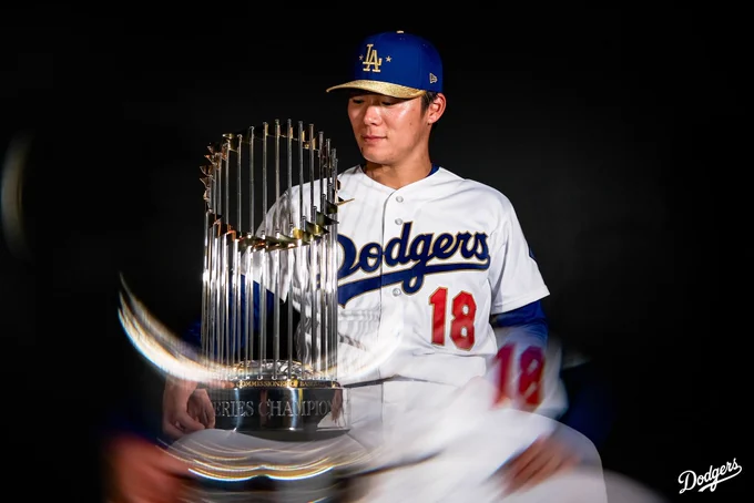 A photo of Yoshinobu Yamamoto wearing the Dodgers gold jersey while holding the World Series trophy.