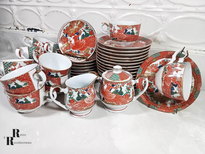 Arita Imari Red Peacock Japanese porcelain set with cups, saucers, small plates, sugar, and creamer, scalloped edges, red and green peacocks, cherry blossoms, and gold trim on a white surface.