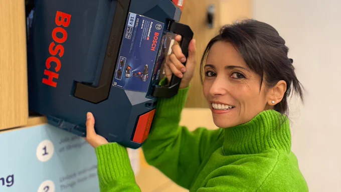Woman in green sweater holding a Bosch tool case, smiling at the camera.