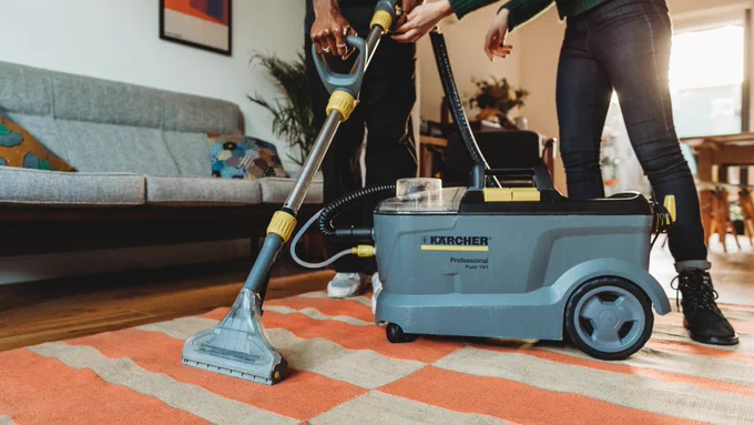 Two people using a Kärcher carpet cleaner on a striped rug in a living room.