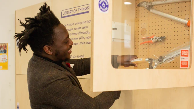 Man smiling while selecting a tool from a "Library of Things" display cabinet.