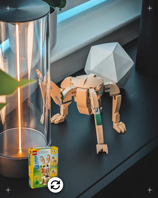 On a metal shelf sits a small, tan creature— five slender appendages end in rocky tips connecting to a chunky, stone, cone-like core. The creature places one of its arms against a glass tube with a line of neon glowing light. The creature stands on a metal shelf, surrounded by artificial plants and a polygonal paperweight.