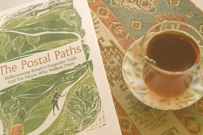 A copy of The Postal Paths next to a drink