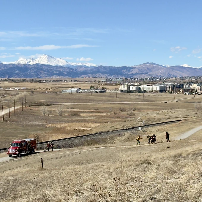 Image of a dry grassy field with a red fire engine and mountains in the background