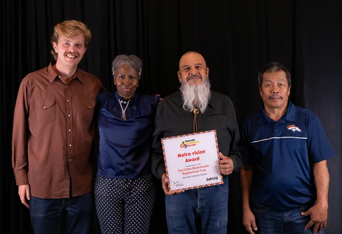 Four adults of various ages and backgrounds pose for a photo. One of them holds an award placard.